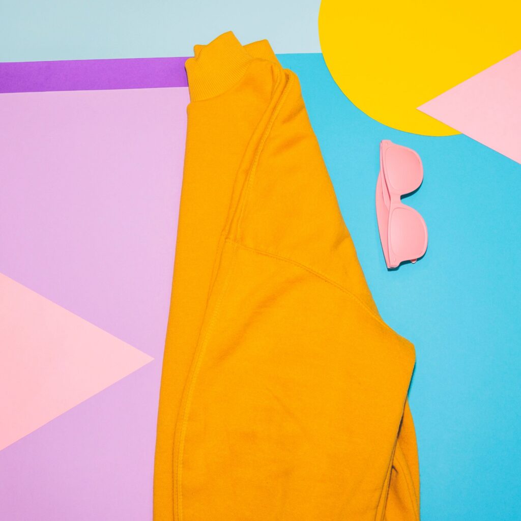 Woman's yellow pullover with pink sunglasses on memphis style background.