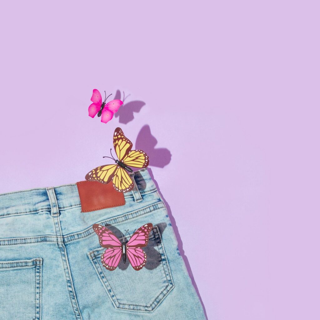 Spring creative layout with faded jeans and colorful butterflies on pastel purple background. 80s or 90s retro romantic aesthetic fashion idea. Minimal romantic summer flat lay.
